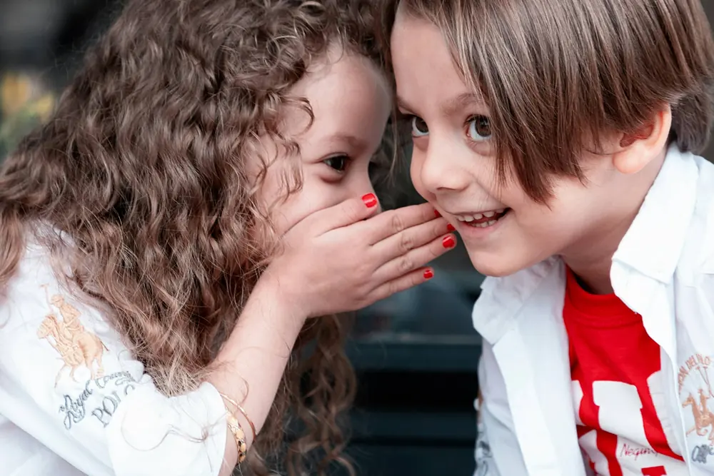 Zwei Kinder flüstern sich etwas ins Ohr